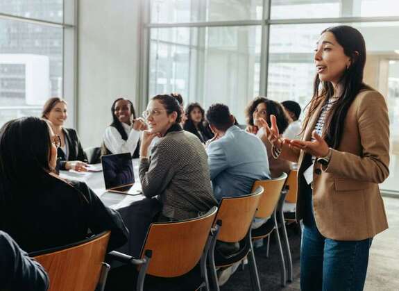 Frau steht vor größerer Gruppe mit Männern und Frauen und erklärt 