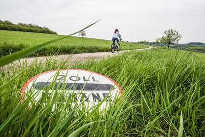 Ein rundes Schild liegt im Gras, auf dem Schild steht "ZOLL DOUANE"
