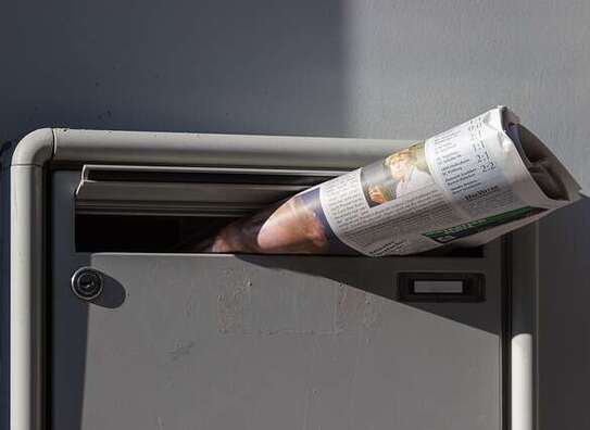 Briefkasten, aus dem einen zusammengefaltete Zeitung herausschaut