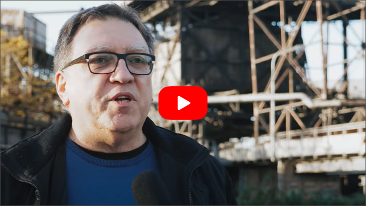 Foto: Videovorschaubild, ein älterer Herr, im Hintergrund Industrieanlagen und Metallgerüste